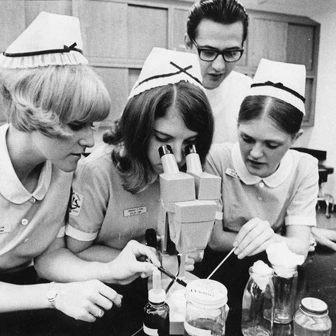 One Nursing student looking in microscope with three other nursing students around her in 1960.