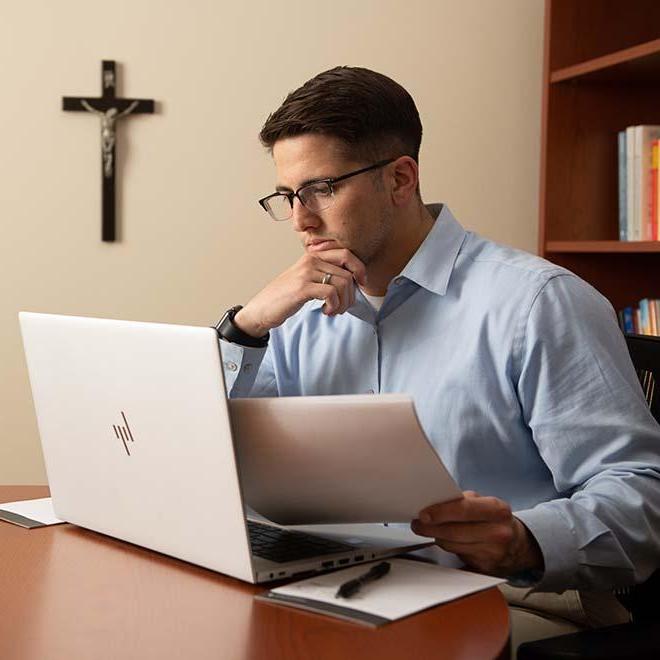 Young professional working on laptop with crucifix in background