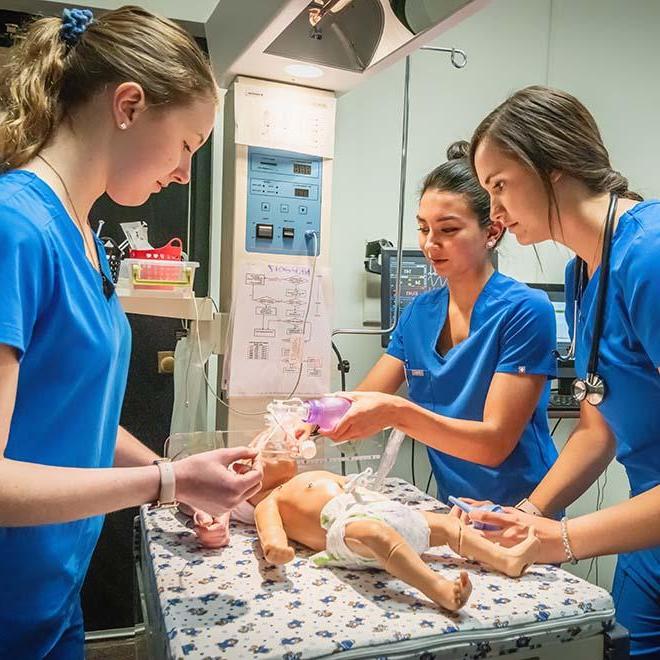 Three nursing students giving breathing treatment to baby mannequin
